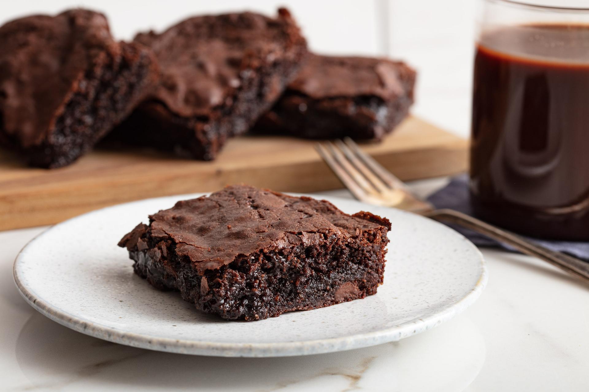 Fudgy chocolate brownies on a speckled plate with a glass of cold brew coffee