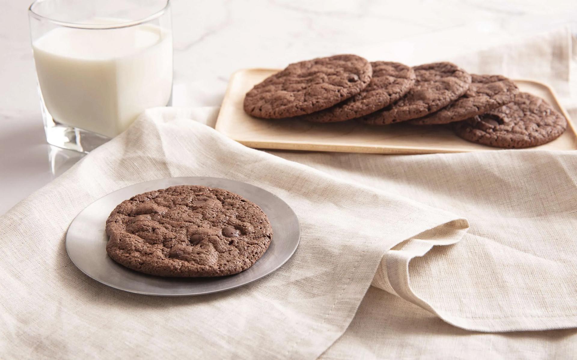 Double chocolate cookies on a pewter plate and wood board with a glass of milk