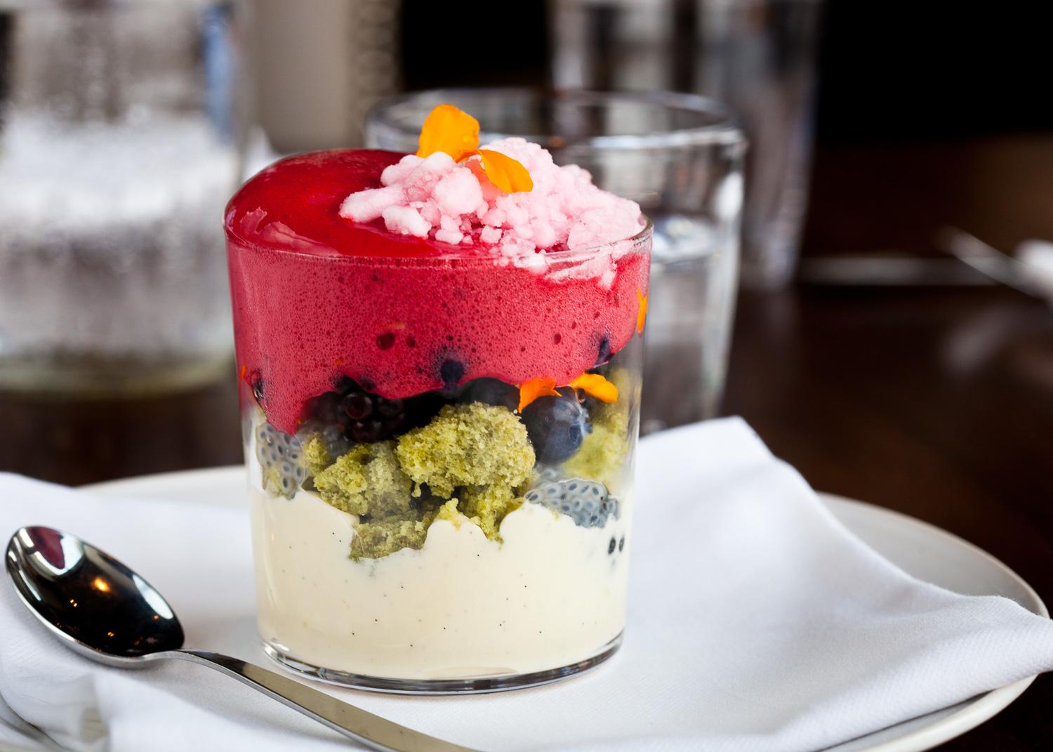 Layered dessert in a glass with vanilla panna cotta, pistachio sponge, blueberries, and red berry foam