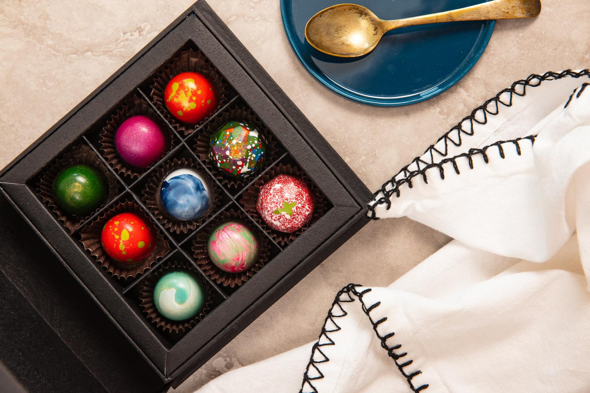 Boxed set of hand-painted artisan bonbons in jewel tones with a gold spoon and linen