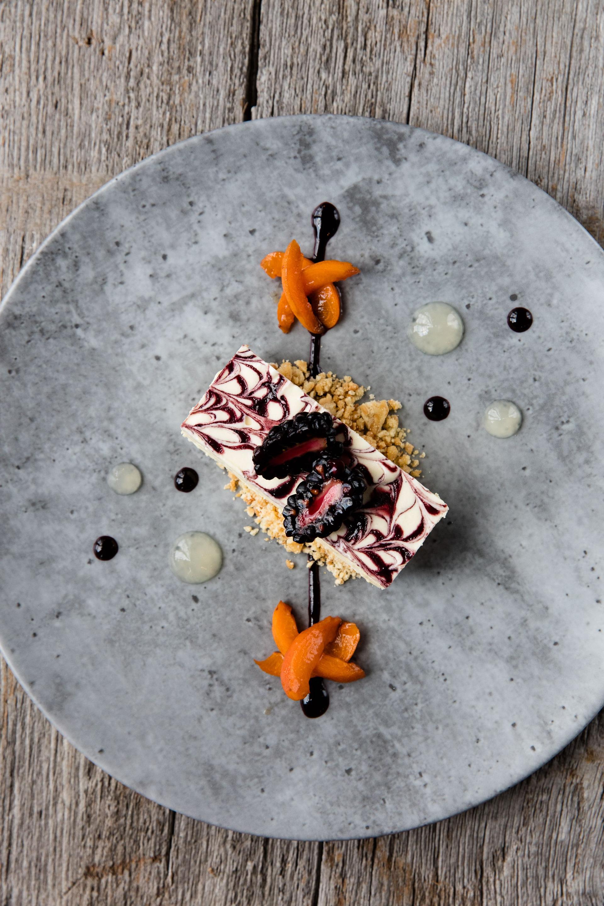 Overhead white chocolate swirl cheesecake with apricot and blackberry on a concrete plate at The Hill