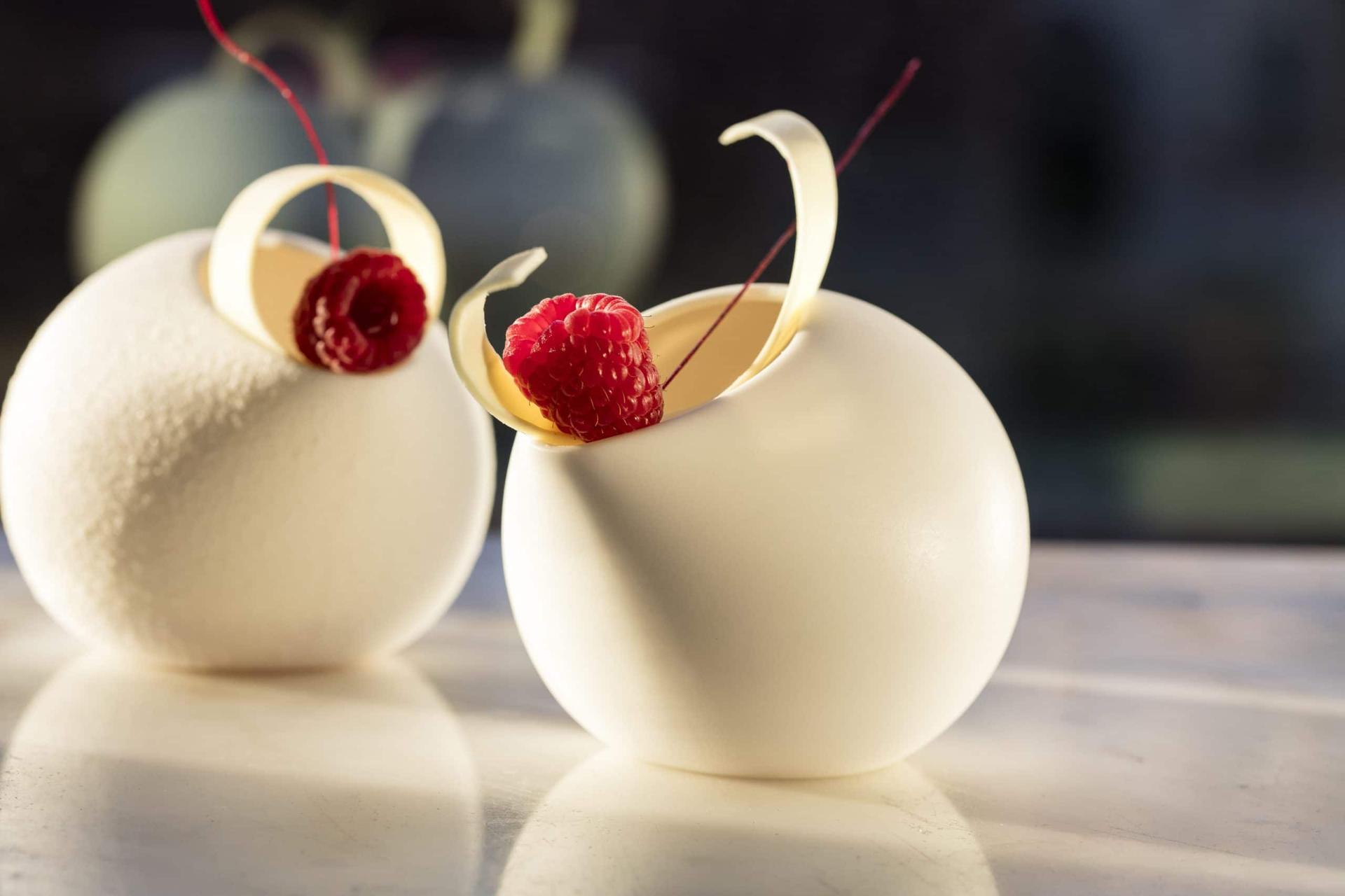 Two white chocolate dome desserts with chocolate curls and fresh raspberries by pastry chef Dominique Ansel