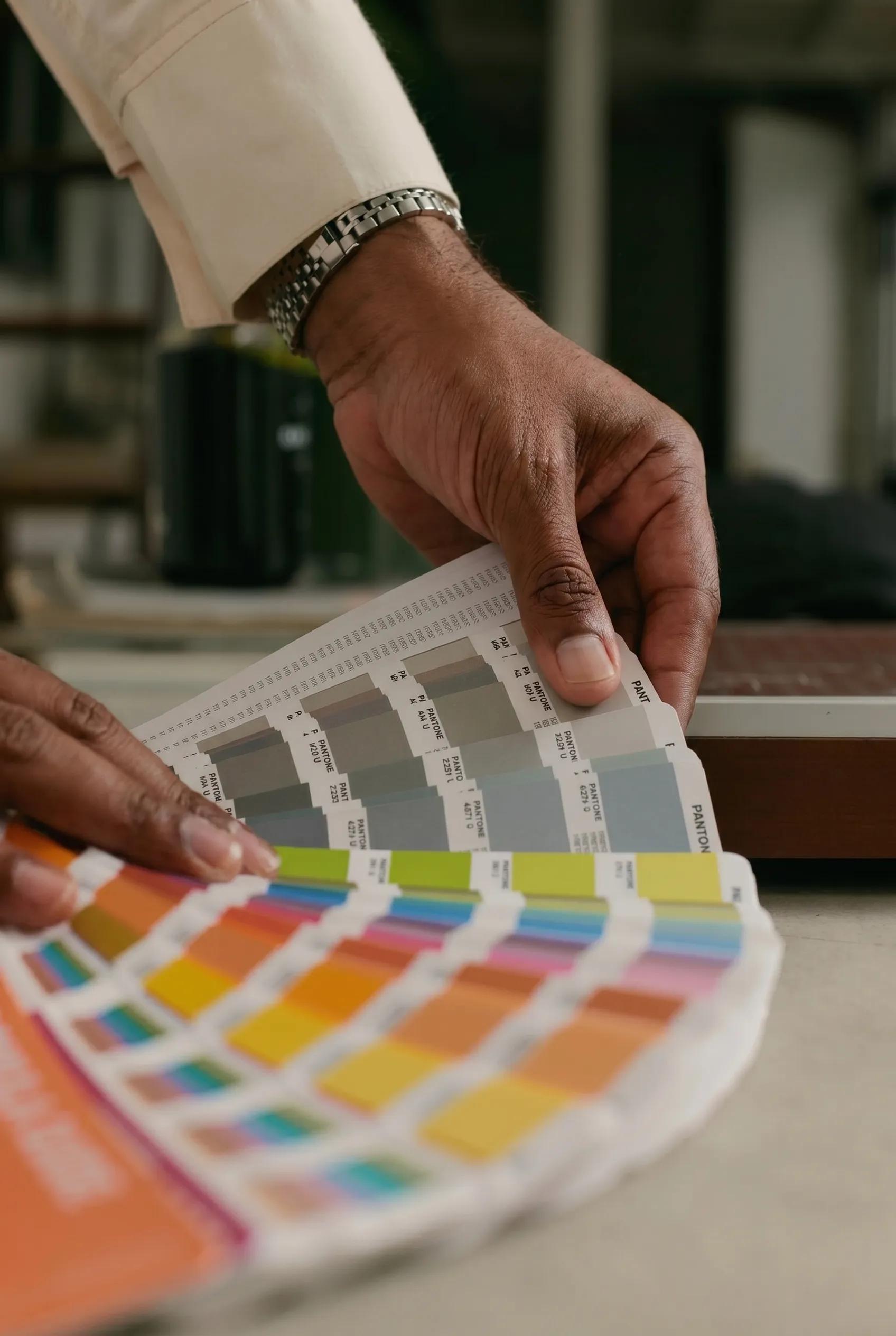 Hands selecting color chips from a Pantone fan, the kind of palette decision that happens in pre-production before a shoot, not after