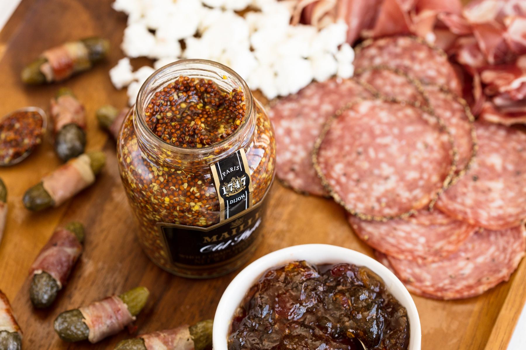 Maille Cornichons jar alongside rustic charcuterie board ingredients