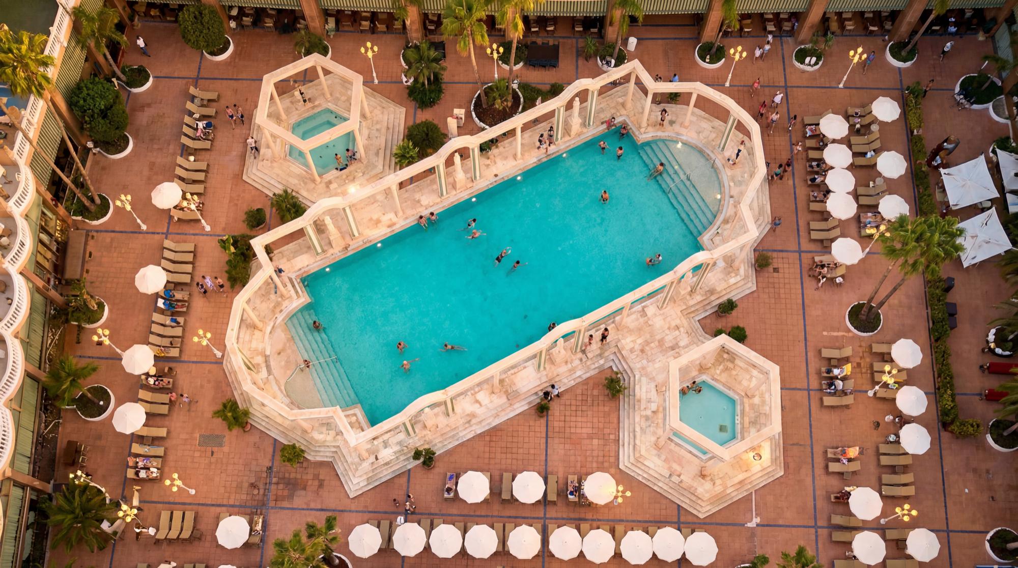 Dramatic top-down drone shot of a luxury hotel infinity pool and lounge deck