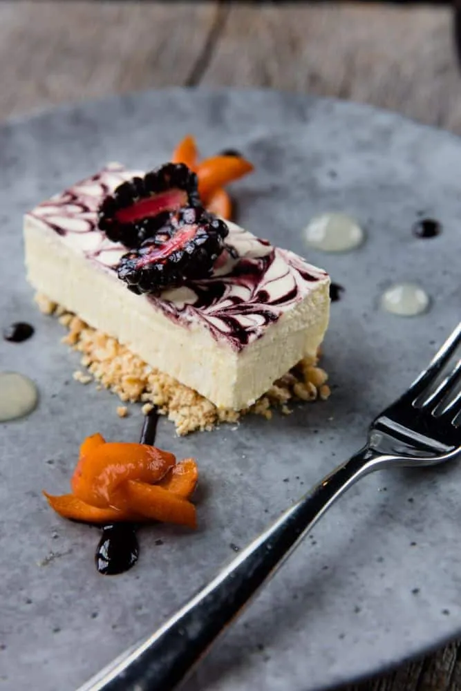 Dessert photographer Brent Herrig captured this rectangular slice of blackberry swirled cheesecake. It sits upon a grey plate.