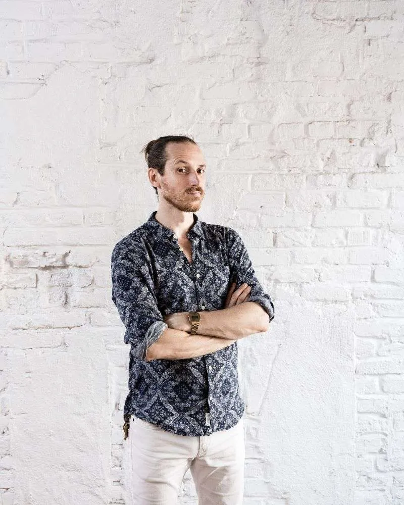 Portrait of Michelin-starred chef Gabe McMackin, standing with crossed arms against a backdrop of whitewashed brick.
